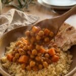 A close-up of a spoon lifting a scoop of chickpea and sweet potato stew over couscous in a bowl.