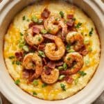 A close-up of a spoon lifting creamy shrimp and grits from a bowl, showing a cheesy texture and savory sauce.