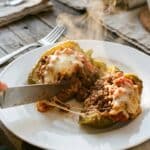 A close-up of a knife cutting into a cooked stuffed pepper, revealing the steaming beef and rice filling.