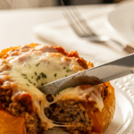 A close-up of a knife cutting into a cooked stuffed pepper, revealing the steaming beef and rice filling.