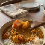 A close-up of a spoon lifting creamy vegetable curry and rice from a bowl, showing tender sweet potato and cauliflower.