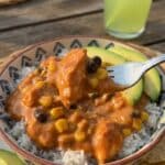 A close-up of a fork lifting a bite of creamy southwest chicken and rice from a bowl with avocado.