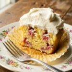 An overhead flat lay of baking ingredients including a basket of strawberries, heavy cream, mascarpone, and eggs.