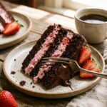 A close-up side view of a slice of chocolate cake showing the pink strawberry filling layers.