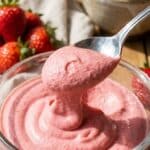 A glass cup filled with smooth, whipped pink strawberry mousse topped with fresh fruit and crumbs