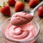 A close-up of a spoon lifting a bite of thick, creamy pink strawberry mousse.