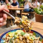 A close-up POV shot of a fork lifting a mixed bite of chicken, rice, and creamy street corn from a bowl.