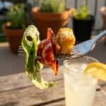 A close-up of a fork lifting a bite of salad with bacon, tomato, and creamy dressing.