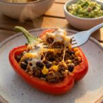 A close-up of a cut-open stuffed red pepper showing the beef and rice filling, with a fork lifting a bite.