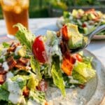 A close-up of a fork lifting a bite of creamy BLT salad with bacon, tomato, and avocado.