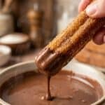 Close-up of a hand dipping a crispy churro into chocolate sauce.