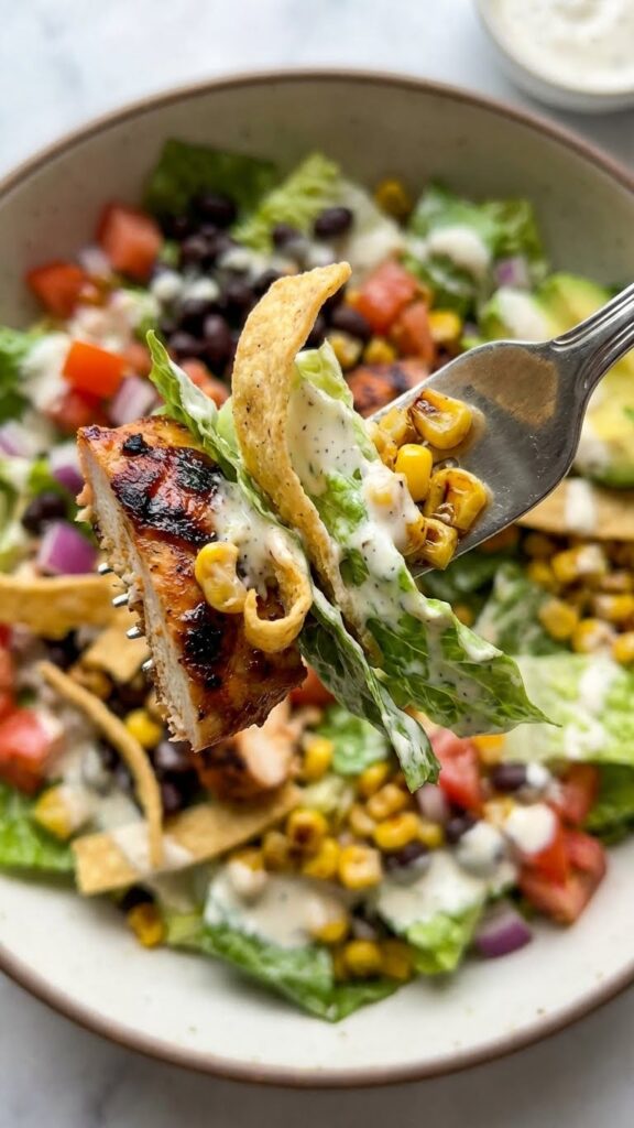 Close-up of a forkful of BBQ chicken salad with ranch dressing and a tortilla strip.