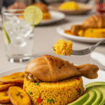 A plate of Arroz Con Pollo served with fried plantains and avocado, with a fork lifting a bite of chicken and rice.