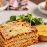 A slice of Baked Spaghetti served on a plate with garlic bread and salad at a cozy dinner table.