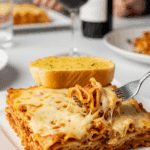 A plate of baked ziti served with garlic bread, with a fork lifting a cheesy bite, set in a cozy dinner atmosphere with red wine.