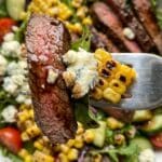 Close-up of a fork holding a piece of steak, gorgonzola cheese, and corn.v