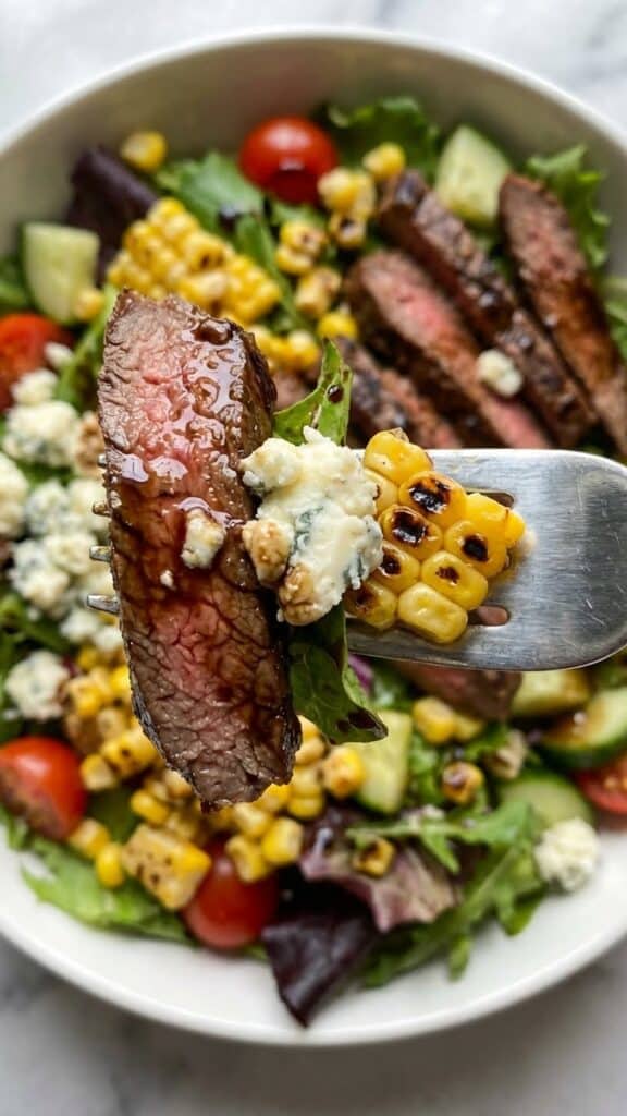 Close-up of a fork holding a piece of steak, gorgonzola cheese, and corn.v