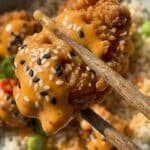 Close-up of a piece of crispy chicken coated in creamy Bang Bang sauce held by chopsticks.