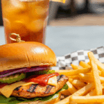 Plated Barbecue Chicken Sandwich served outdoors with fries and iced tea.