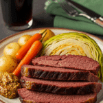 Plated Braised Corned Beef Brisket slices with vegetables, mustard, and a pint of stout beer in a cozy setting.