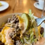 Close-up of a forkful of burger bowl ingredients covered in sauce.