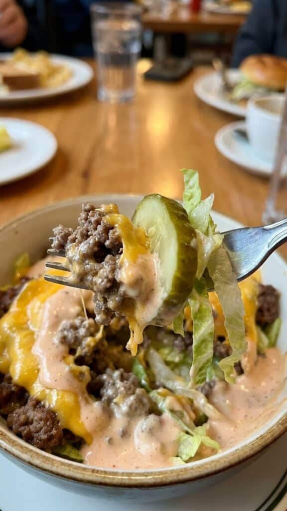 Close-up of a forkful of burger bowl ingredients covered in sauce.