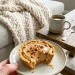 A hand holding a bitten Butterfinger mini pie on a plate with coffee in the background.