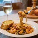 Plated Cajun Seafood Pasta with a fork lifting noodles, served with garlic bread and white wine at a dinner table.