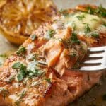 Close-up of a fork holding a buttery, flaky piece of herb-crusted salmon.