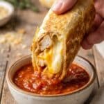 Close-up of a crispy garlic chicken wrap being dipped in marinara sauce.