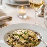 Plated Mushroom Risotto in a shallow bowl, garnished with Parmesan and chives, served with white wine.