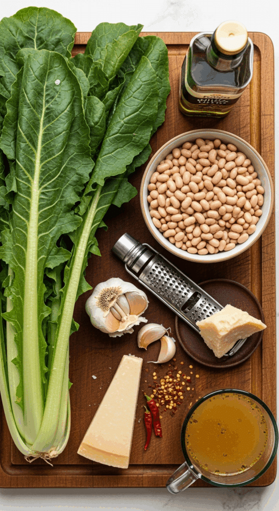 Overhead view of ingredients for beans and greens: fresh escarole, white beans, lots of garlic, olive oil, parmesan, and chili flakes on a wooden board.