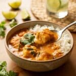 A bowl of creamy Brazilian fish stew served over white rice, with a spoon lifting a bite of fish, set in a warm tropical dining atmosphere.