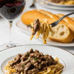 Plated Beef Stroganoff served with a glass of red wine and crusty bread in a candlelit setting.