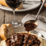 Plated Coq au Vin served over mashed potatoes in a bowl with bread and a glass of red wine.