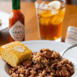 Plated Red Beans and Rice served with cornbread and hot sauce on a wooden table.