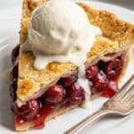 Close-up of a slice of cherry pie à la mode with a scoop of melting vanilla ice cream.