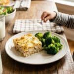 A serving of cheesy chicken tater tot casserole on a plate with a side of steamed broccoli.