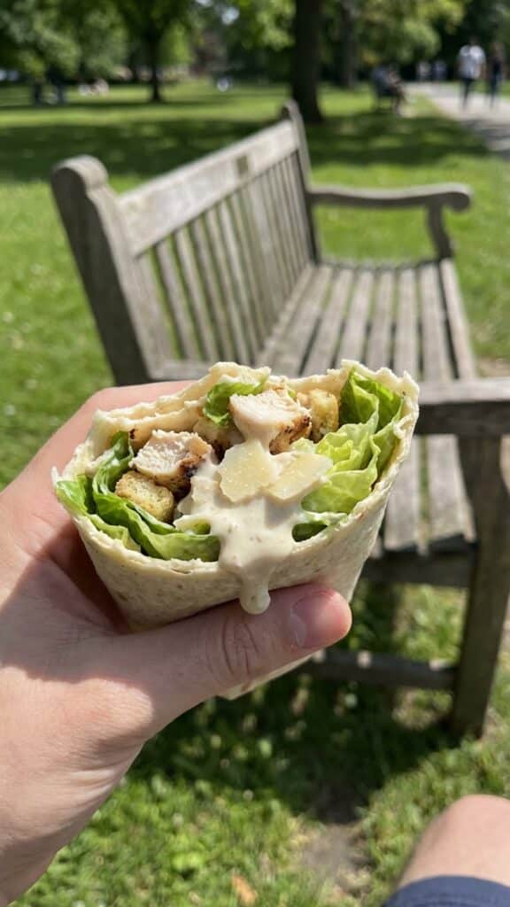 A hand holding a chicken Caesar wrap with a bite taken out of it.