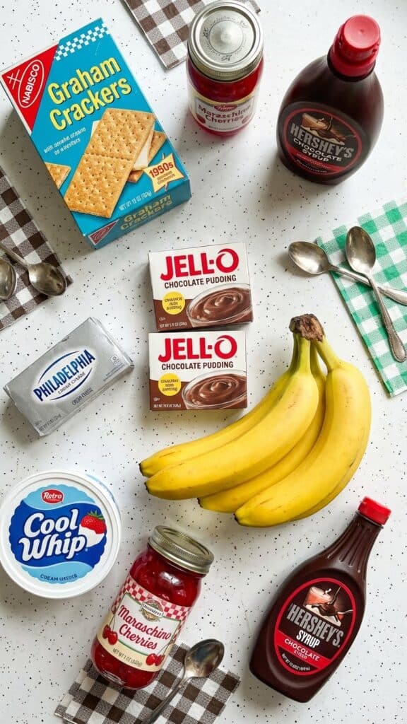 Ingredients for banana split cake including bananas, pudding mix, cherries, and graham crackers.