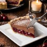 A slice of creamy chocolate cherry pie served on a plate with red wine in the background.