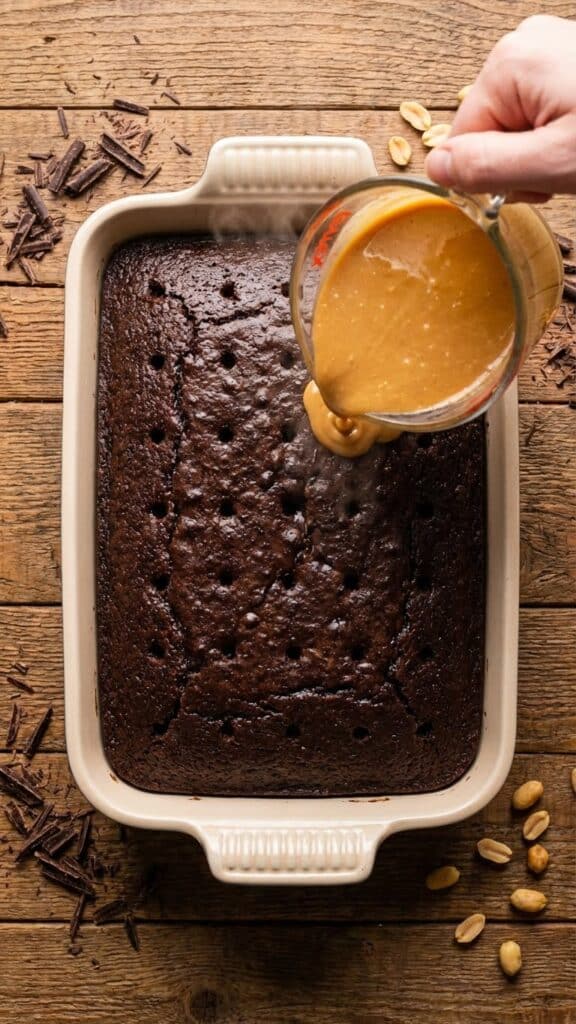 Pouring peanut butter sauce into the holes of a chocolate cake.
