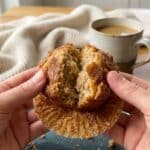 A close-up of hands breaking open a warm cinnamon sugar muffin, showing steam rising and the sugary crust cracking.
