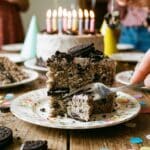 A slice of Oreo cake served at a birthday party with confetti and balloons.
