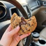 A hand holding a bitten frosted cotton candy cookie inside a car.