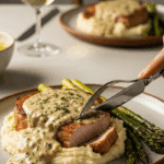 Plated Creamy Herbed Pork Chop served over mashed potatoes with asparagus at a dinner table.