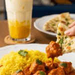 Plated Chicken Tikka Masala with pilau rice, with a piece of naan bread dipping into the sauce.