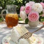 A slice of coconut cake served on a floral plate with iced tea in the background.
