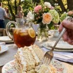 A slice of coconut cake served on a floral plate with iced tea in the background.