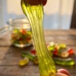Close-up of a hand stretching a cAhewy pickle gummy worm.
